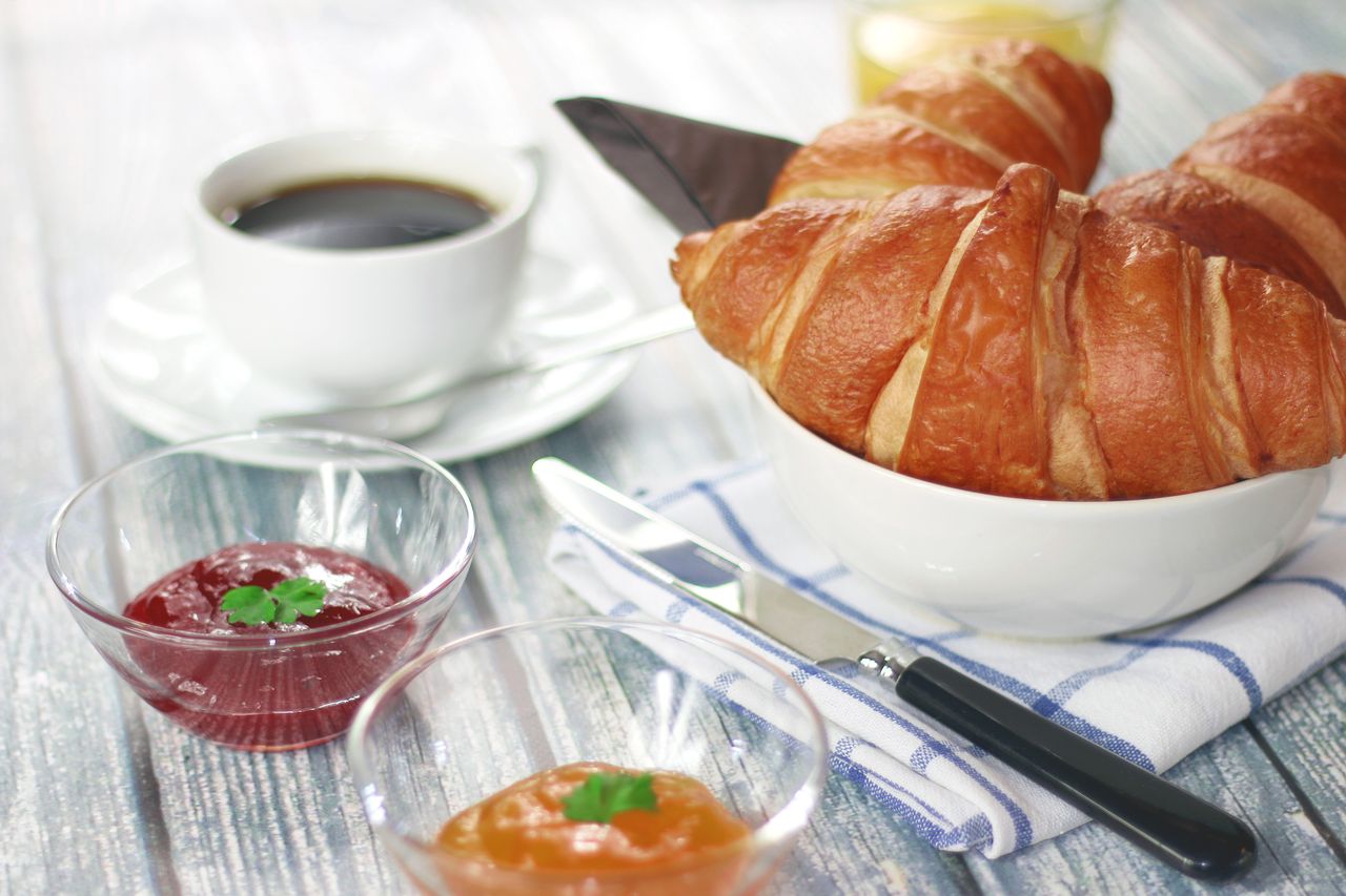 Home Delicious breakfast featuring croissants, coffee, and assorted jams on a rustic table.