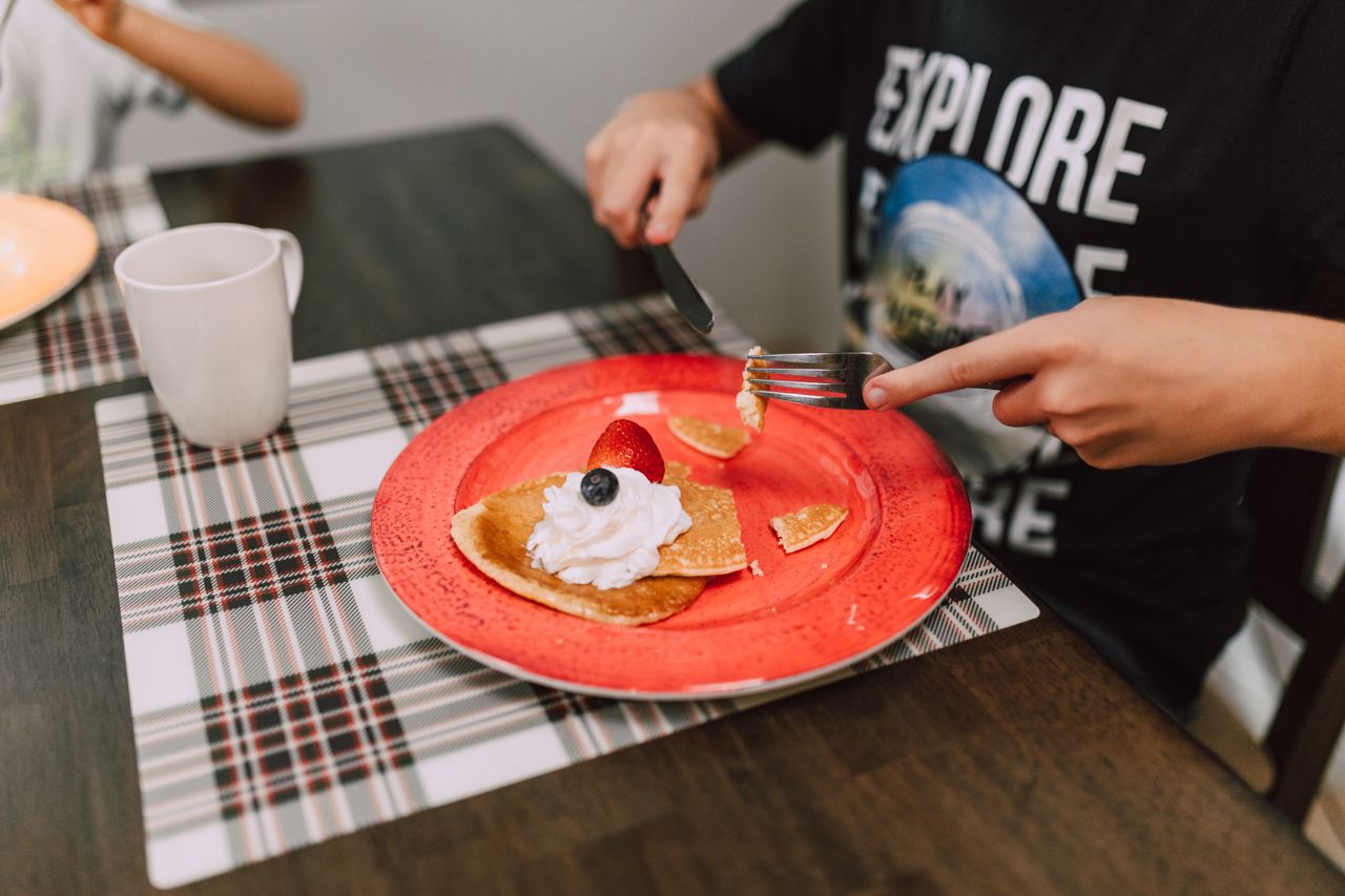 Offerings Pancakes served with whipped cream and fruit on a vibrant red plate. Perfect breakfast setting.